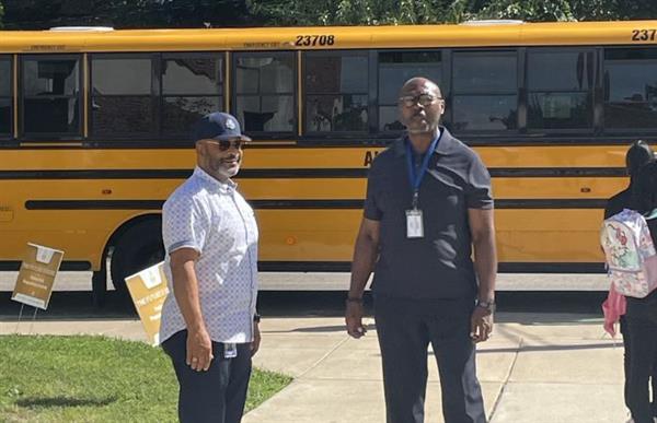 two men standing outside of a school bus
